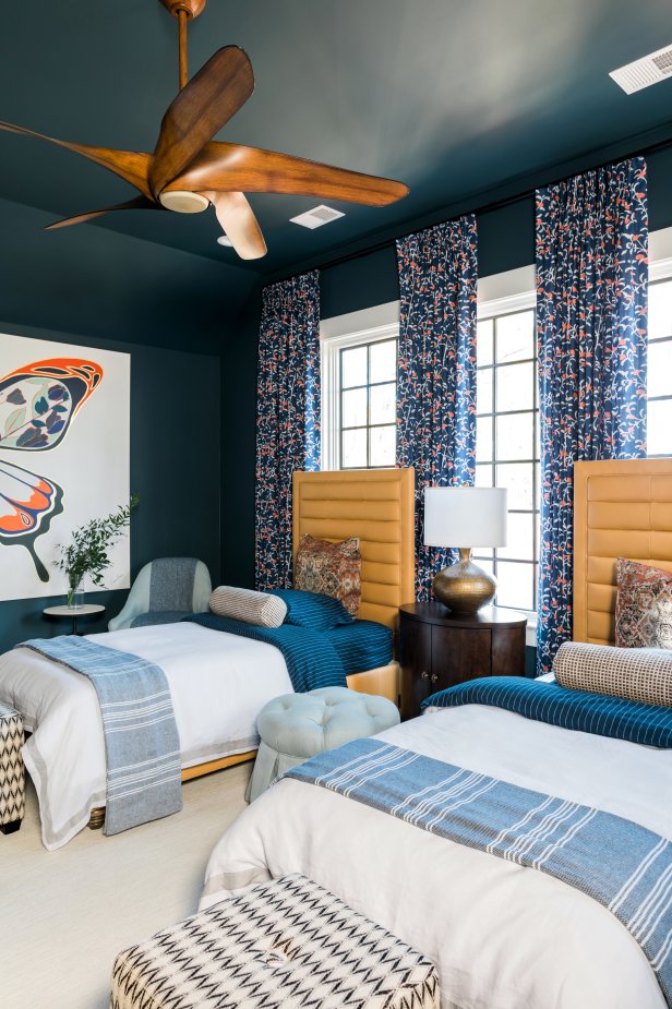 Blue floral curtains stand out against the blue walls in this teen bedroom. A vintage-style fan adds a touch of midcentury-modern flair to the transitional space, which also includes custom leather headboards and custom artwork.