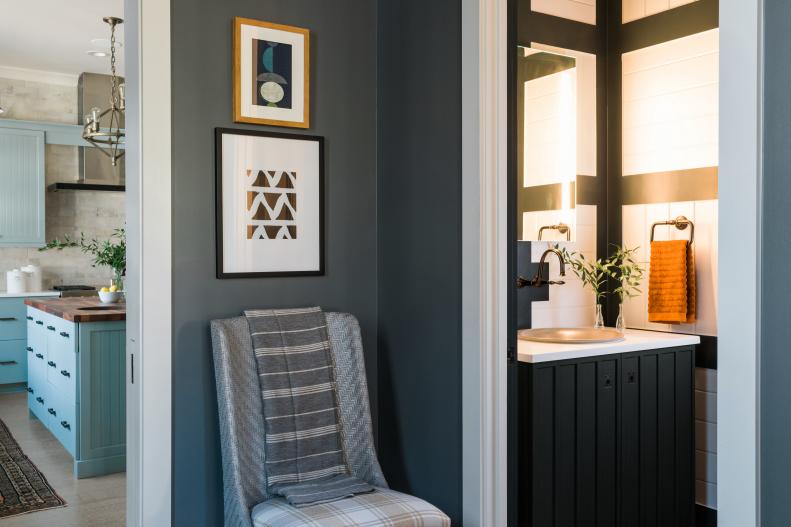 This angle shows how the mudroom shares an easy connection with the kitchen and powder room. A woven chair with a striped throw blanket in the mudroom offers a spot to rest or remove shoes, with framed art above decorating the wall.