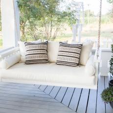 White Farmhouse Front Porch with an Upholstered White Swing 