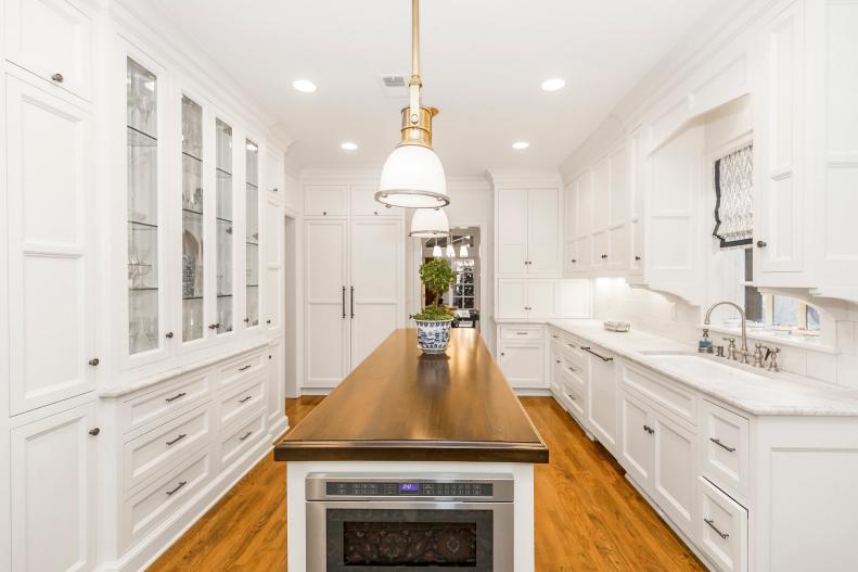 This crisp white galley kitchen features an island with a wood top. 