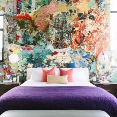 Master Bedroom With Colorful Abstract Accent Wall And Purple Bed Linens