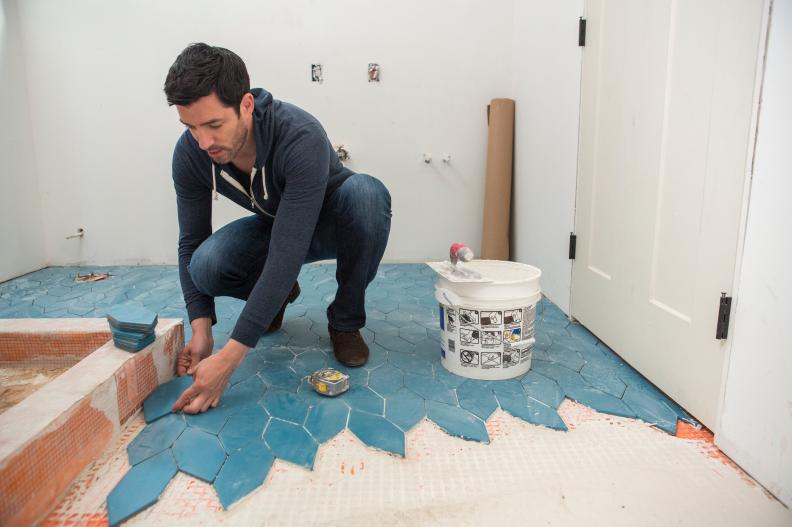 Host Drew Scott installs floor tiles in a bathroom, as seen on Brother vs. Brother.