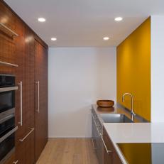 Modern Galley Kitchen With Stainless Steel Sink And Work Space With Yellow Glass Backsplash
