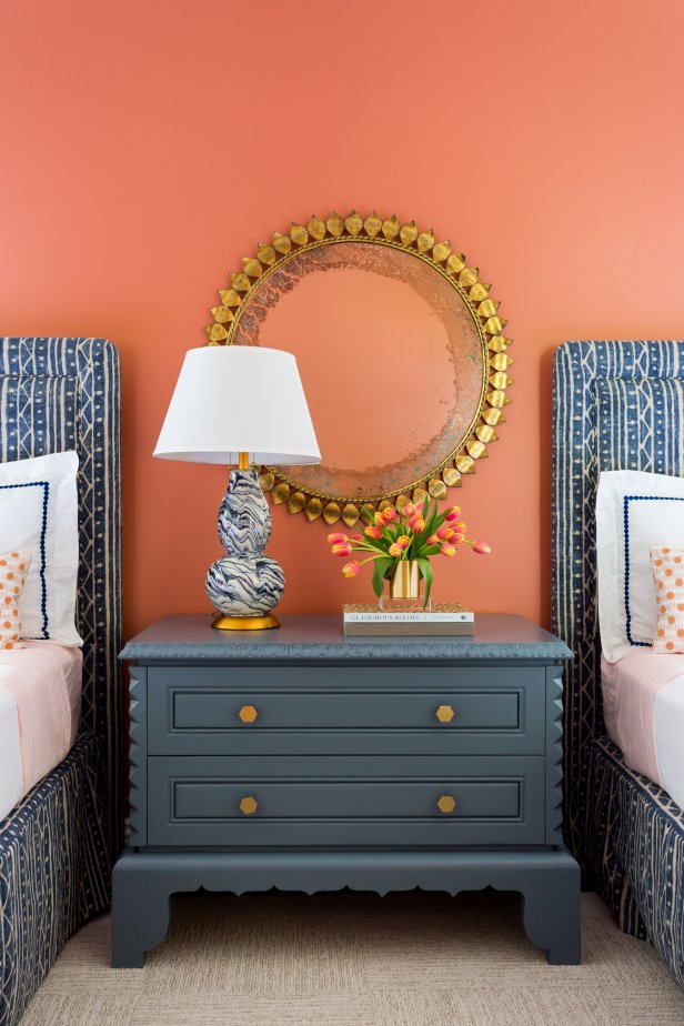 An orange accent wall instantly infuses this guest bedroom with warmth. The space also features two blue-patterned frames, a large dresser and a marbled lamp for reading into the evening.