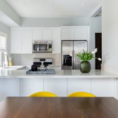 Modern Open Concept Kitchen And Dining Area With White Cabinets And Walls And Pops Of Yellow