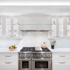 Traditional White Kitchen With Glass Front Cabinets And Stainless Steel Gas Range With White Vent Hood