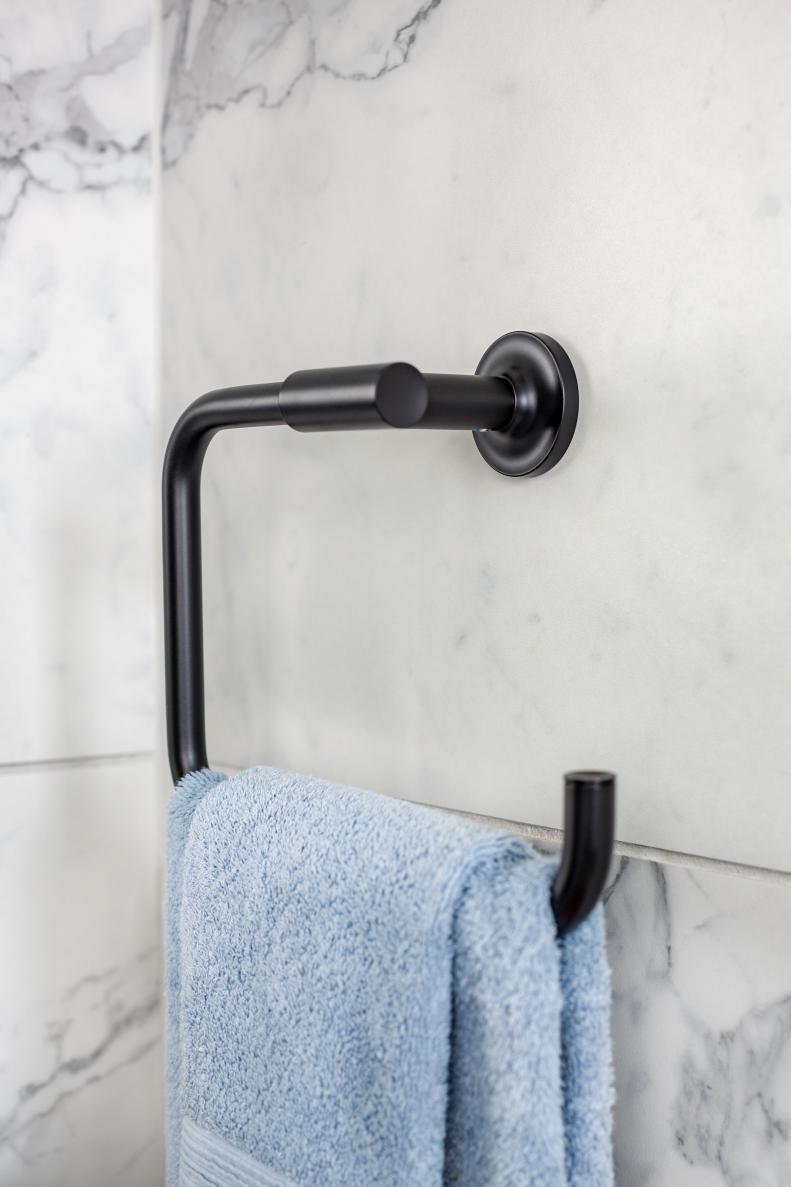 A sleek black towel bar echoes the design of the faucet and pops against the marble style porcelain tiles.