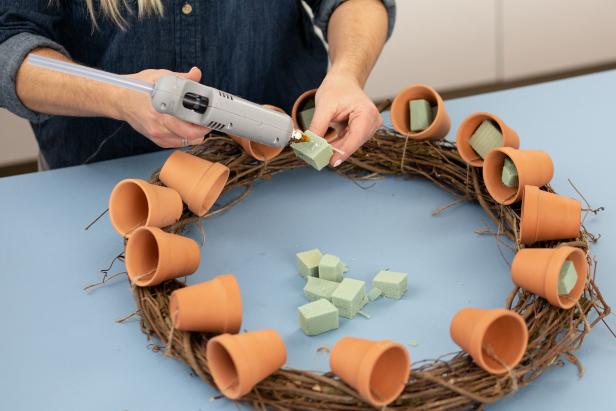 Cut floral foam into cubes small enough to fit inside the pots. Attach to the inside of the pot with hot glue. Attach two cubes to each pot if necessary.