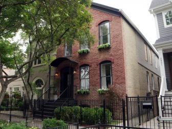 The completed exterior of the Lincoln Park Fourplex remodeled on Windy City Rehab features a refinsihed entrance with a stylish black arch, brand new black framed windows, charming window boxes, and lush new landscaping.
