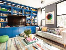 Why settle for one amazing living room when you can have two? Taking full advantage of his home’s layout, Rayman created this second living area to showcase his love of color. Here he takes the tightly condensed color and pattern of the living area at the front of the space and stretches it out across the rug, pillows and art of this larger room. At the center of it all is a stunning bookcase, a tribute to the designer’s favorite color. Drawing on his expertise and connections, he had the unit custom built in small sections so that they could be assembled quickly once in place.