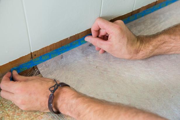 Directly onto the subfloor, lay down a layer of plastic sheeting to create a moisture barrier. Tape the sheeting two inches above the floor using painter's tape.