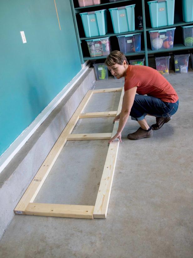 Begin building the base of the cabinets on the ground by laying out two 8-foot 2x4 boards on the floor parallel to the wall. Next, cut four 32-inch 2x4 boards and place them perpendicular between the 8-foot pieces on each end and two in the middle.