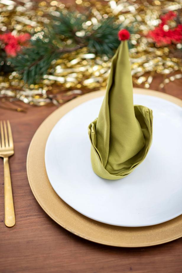 Elf Shaped Napkin Sitting on Plate With Gold Silverware