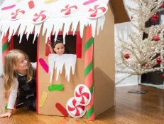 A Little Girl Playing in a Gingerbread House With a Doll