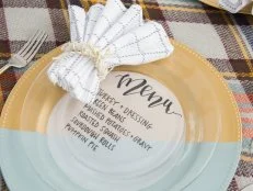 A Gold Charger on a Tablecloth With a Menu and Napkin