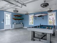 This wide view inside the garage shows the user-friendly layout, with multiple ceiling fans for keeping the space cool during warm days and nights. The garage also includes framed windows that allow natural light inside and offer views of the surrounding property. A paddle board on a wall mounted rack offers the chance to enjoy the water activities in the area.