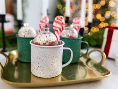 Gold tray with hot cocoa ornaments and peppermint spoons in mugs.