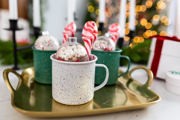 Gold tray with hot cocoa ornaments and peppermint spoons in mugs.