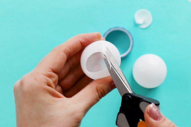 Begin by cutting a circle in the top and bottom of one ping pong ball. Then, use hot glue to glue it on top of another ping pong ball.
