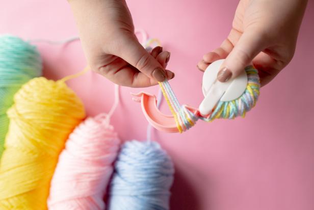 To make a multicolored pom-pom, begin by wrapping four strands of different-colored yarn around one arm of the pom-pom maker until you reach desired fullness. Close it into the middle once complete. Bring the strands over to the other arm and repeat.