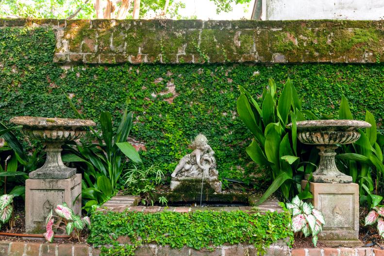 An elegant water feature is bookended by perfectly symmetrical urns which create a kind of stage set that frames this charming garden statue.