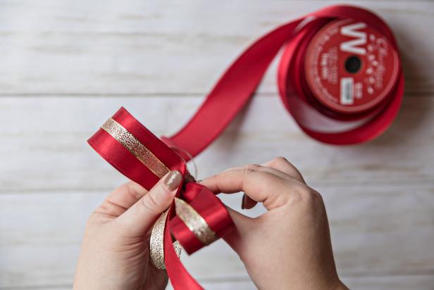 To create a layered bow, place the gold ribbon in the middle of the red ribbon. Starting about 6 inches from the end, fold the ribbons over to create a loop. Next, twist the ribbons 180° so the front of the ribbon is facing up again.