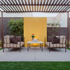 Metal Pergola with Neutral Sitting Area and Yellow Wall 
