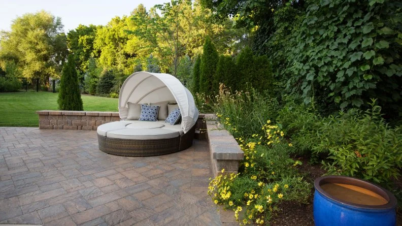 Round Daybed With Retractable Canopy Sits In Corner Of Outdoor Patio 