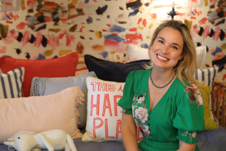 After the renovation, Grace Mitchell poses in the attic bedroom and art nook on the delightful new futon with unique vivaciously colored wallpaper that captures the color scheme used in the rest of the space as seen on One of a Kind.