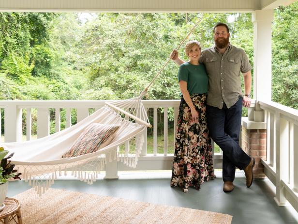 As seen on Home Town, Ben and Erin Napier (R) stand on the covered porch of the newly renovated Guay home in Laurel, Mississippi. On the exterior, the old pipe columns have been removed and new wood columns and decorative railing has been installed.  New paint, landscaping and new porch roofing help to improve the exterior. (portrait)