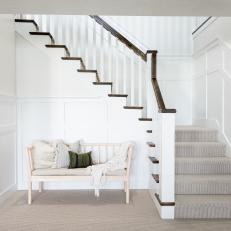 Bench at Base of Staircase With Dark Wood and White Banisters, Striped Wallpaper