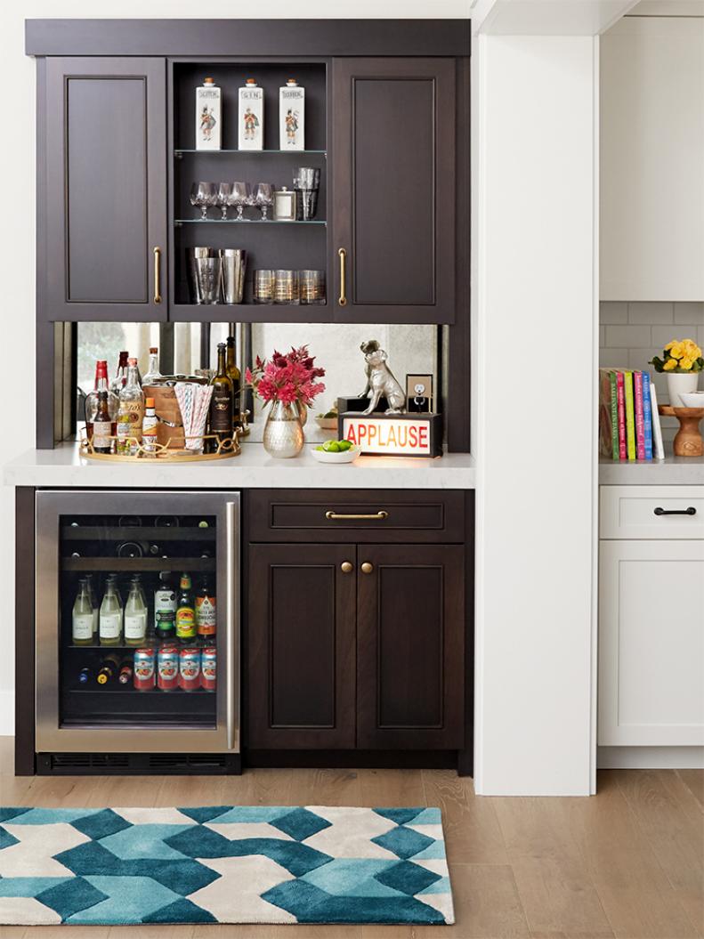 This bar area from HGTV Magazine is tucked between the kitchen and the dining room and features ample shelving and a mini fridge.