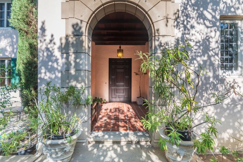 Two Plants Flank A Stone Arch Entryway Leading To The Front Door