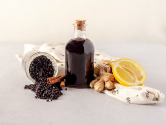 A bottle of elderberry syrup with dried elderberries, ginger, lemon and cinnamon sticks. 