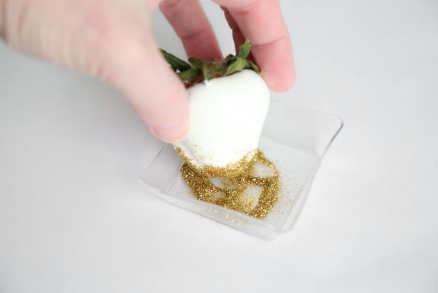 Pour edible gold glitter into a small condiment cup. Lightly coat the tips of five white candy-dipped berries with piping gel or corn syrup. Dip the coated ends of the berries into the glitter. Transfer the berries to parchment paper to dry, about 15 minutes. Transfer each strawberry to a cupcake liner.
