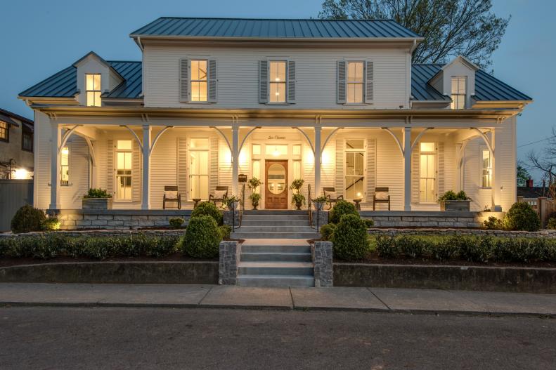 White Farmhouse Has Steps Leading to Warmly Lit Front Porch