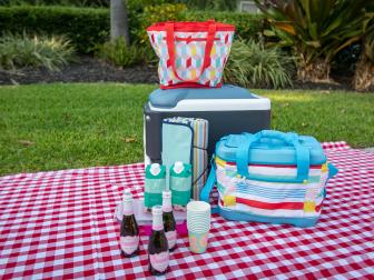 A variety of coolers and champagne on a checkered picnic blanket. 