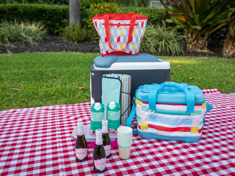 A variety of coolers and champagne on a checkered picnic blanket. 