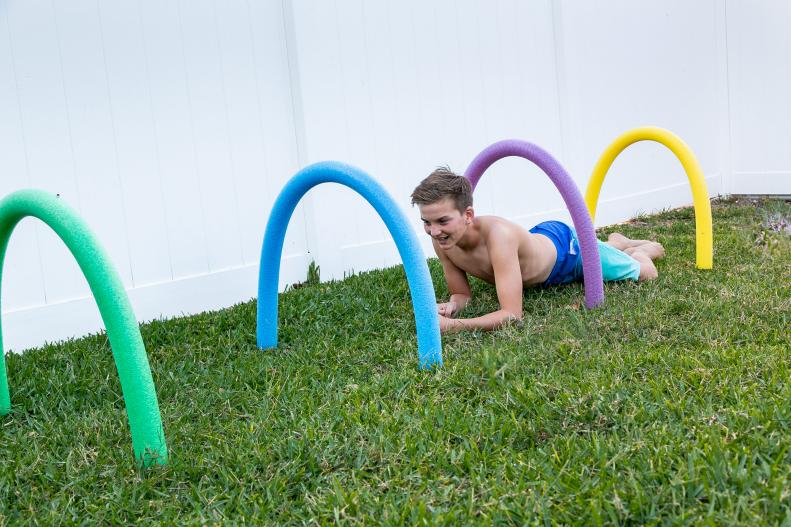 A boy crawls through a backyard obstacle course made from pool noodles. 