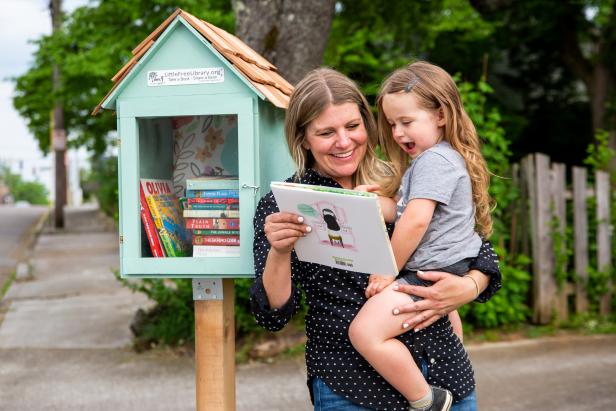 A Child Laughs Beside a Little Free Library While Looking at a Book
