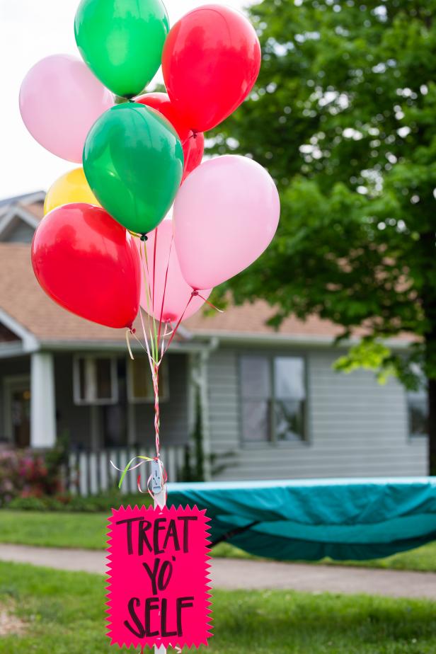 This big bunch of balloons helps to draw attention to the bright sign that is stuck in the ground advertising this yard sale. A table with a bright tablecloth can be seen in the background.