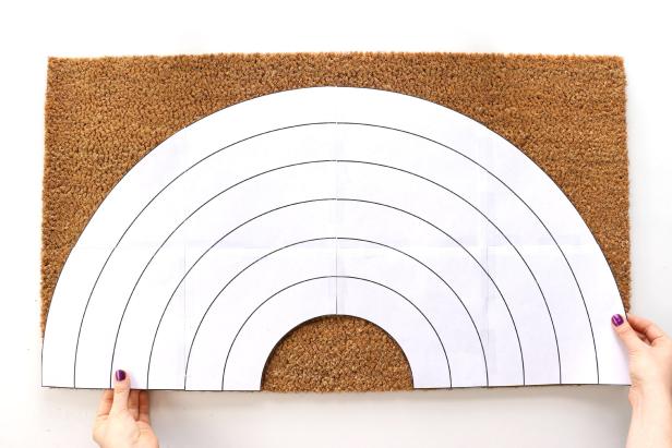 Start with a plain doormat. Print out the rainbow pattern, tape it together and cut out the rainbow shape. Pin it in place using straight pins and trace the pattern with a permanent marker.