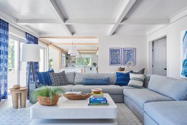 This contemporary living room is awash in all shades of blue, from the soft blue sectional sofa to the cerulean throw pillows to the marine blue artwork and draperies. A coffered beadboard ceiling provides texture and interest overhead, while neutral walls create a calming environment.