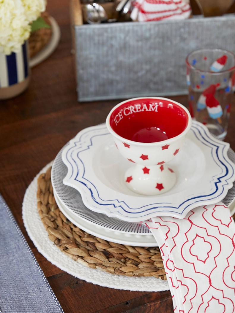 Once you’ve laid the foundation, create a festive place setting. Jenny’s seven-layer place setting formula works for “any occasion this summer,” she says.

To recreate her seven-layer place setting, start with one or two chargers as anchors. Then layer in a large hobnail plate with a melamine or ceramic plate on top. Then Jenny suggests layering in a seasonal dish towel in place of a napkin. “I consistently use dish towels as napkins…layering [them] in between dishware so it drapes off the center of the setting,” she explains. Finally, add a coordinating salad plate and a small dish, bowl or bread plate and a name card or seasonal accessory.
