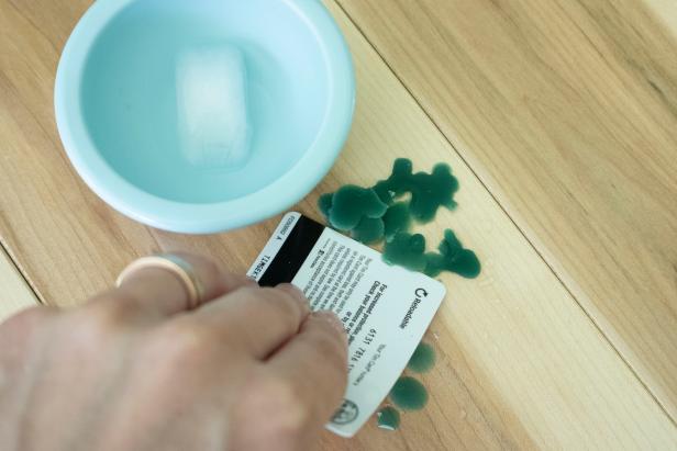 Hand holding a credit card to scrape spilled candle wax on wooden table from HGTV