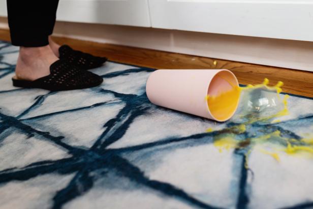 cup of orange juice spilling on blue-and-white rug