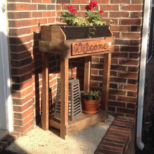 Wooden Planter With Lower Shelf and Welcome Sign Next to Front Door