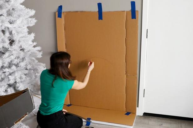 Cut open your cardboard box to get large sheets of cardboard. Tape to the wall and draw your fireplace shape.