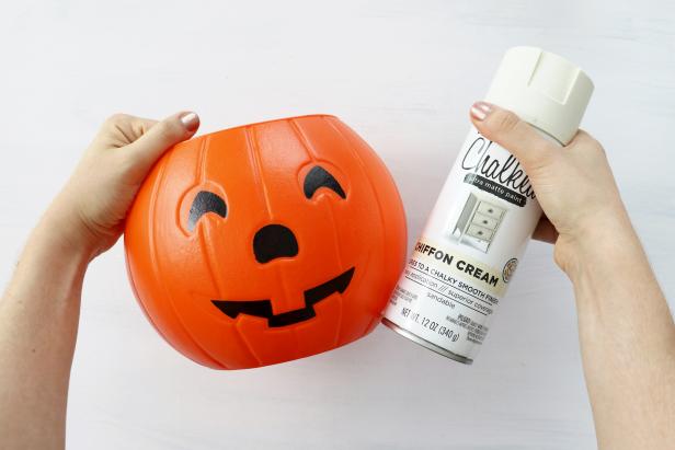 Spray paint a jack-o'-lantern trick-or-treat bucket with off-white spray paint.