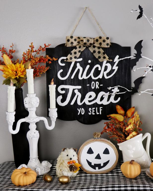 White accents, silk fall foliage and a fun &quot;trick-or-treat yo self&quot; sign topped with a burlap bow create a farmhouse chic Halloween display.